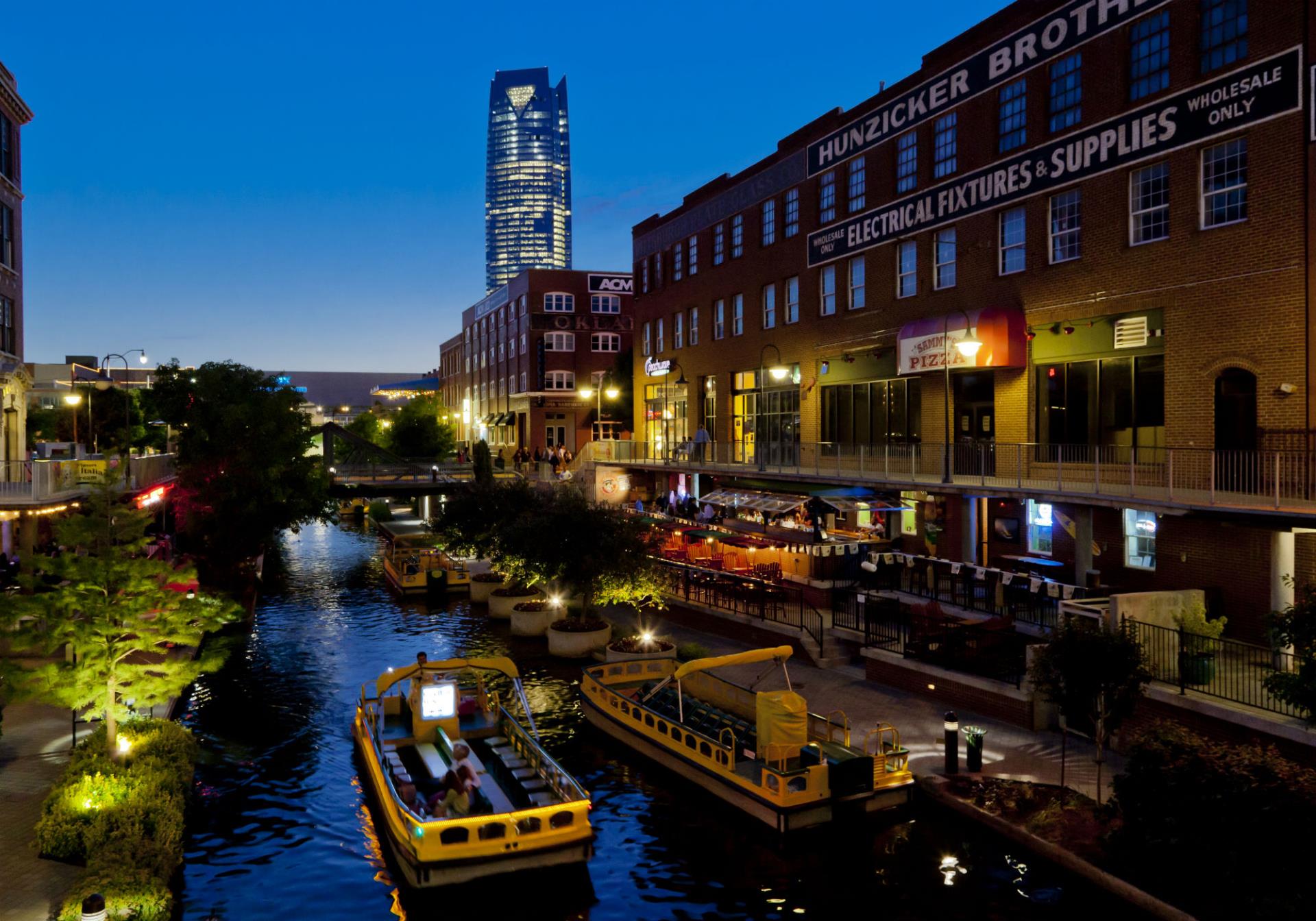 A photo taken at sunset of the Bricktown Canal with an open air boat carrying passengers.