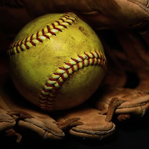 Yellow softball with red stitches sitting inside a brown glove