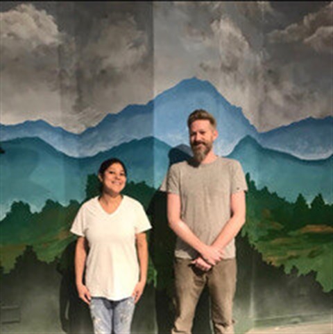 short woman and tall man standing in front of mural
