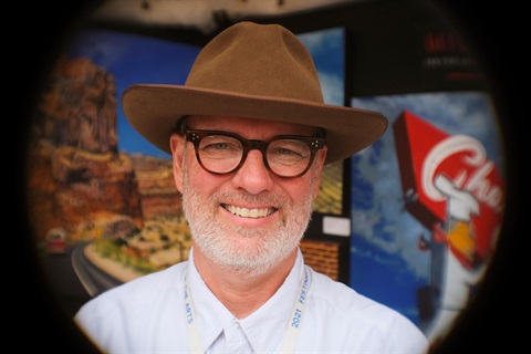 fish eye lense photo of white guy with white beard and white shirt with a brown brimmed hat