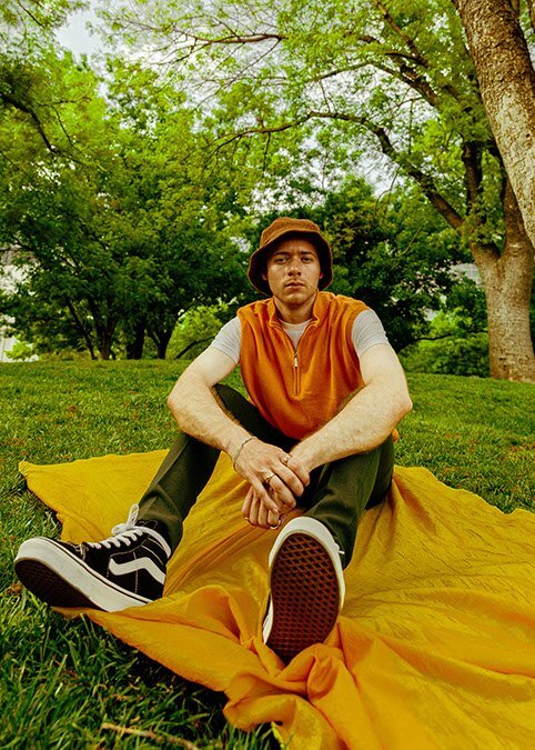 photograph of man sitting on yellow blanket in the park