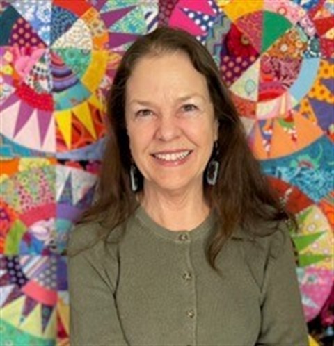 woman in green shirt with brown hair in front of quilt art
