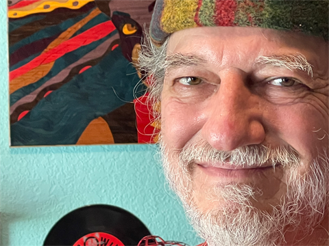 man with gray beard and colorful hat in front of art