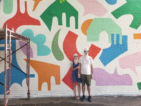 two people wearing white masks standing in front of mural