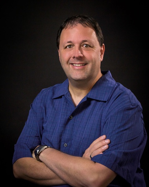 headshot of white man wearing short-sleeved navy shirt