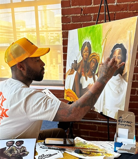 younger black man in yellow ballcap painting on canas on an easel
