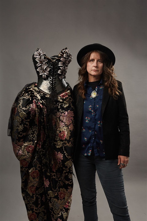 woman in suit and brimmed hat next to ceramic corset and full brocade shirt