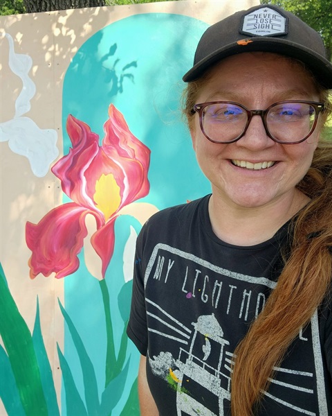 red head woman in ballcap and glasses in front of tulip painting