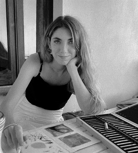 black and white photo of white woman leaning on hand with art supplies in front of her