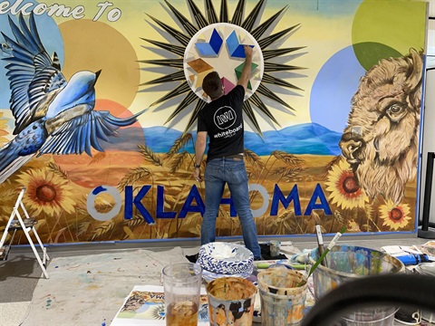 guy in jeans painting welcome to oklahoma mural
