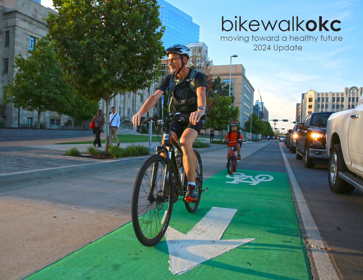 The cover of bikewalkokc. A man is biking in a green striped bike lane, followed by a young boy on a bike. 
