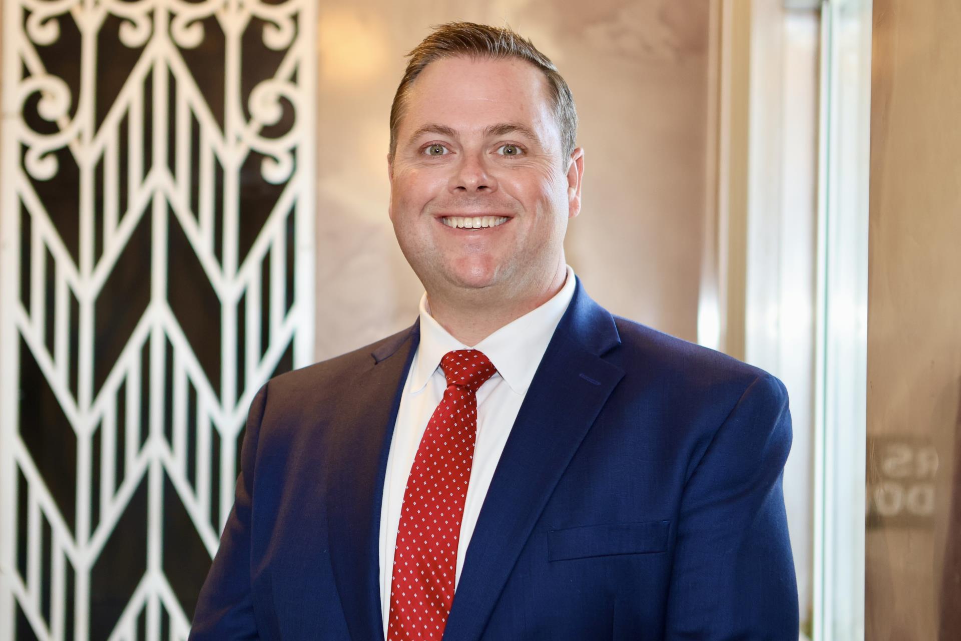 christopher foshee smiling wearing red tie and navy suit
