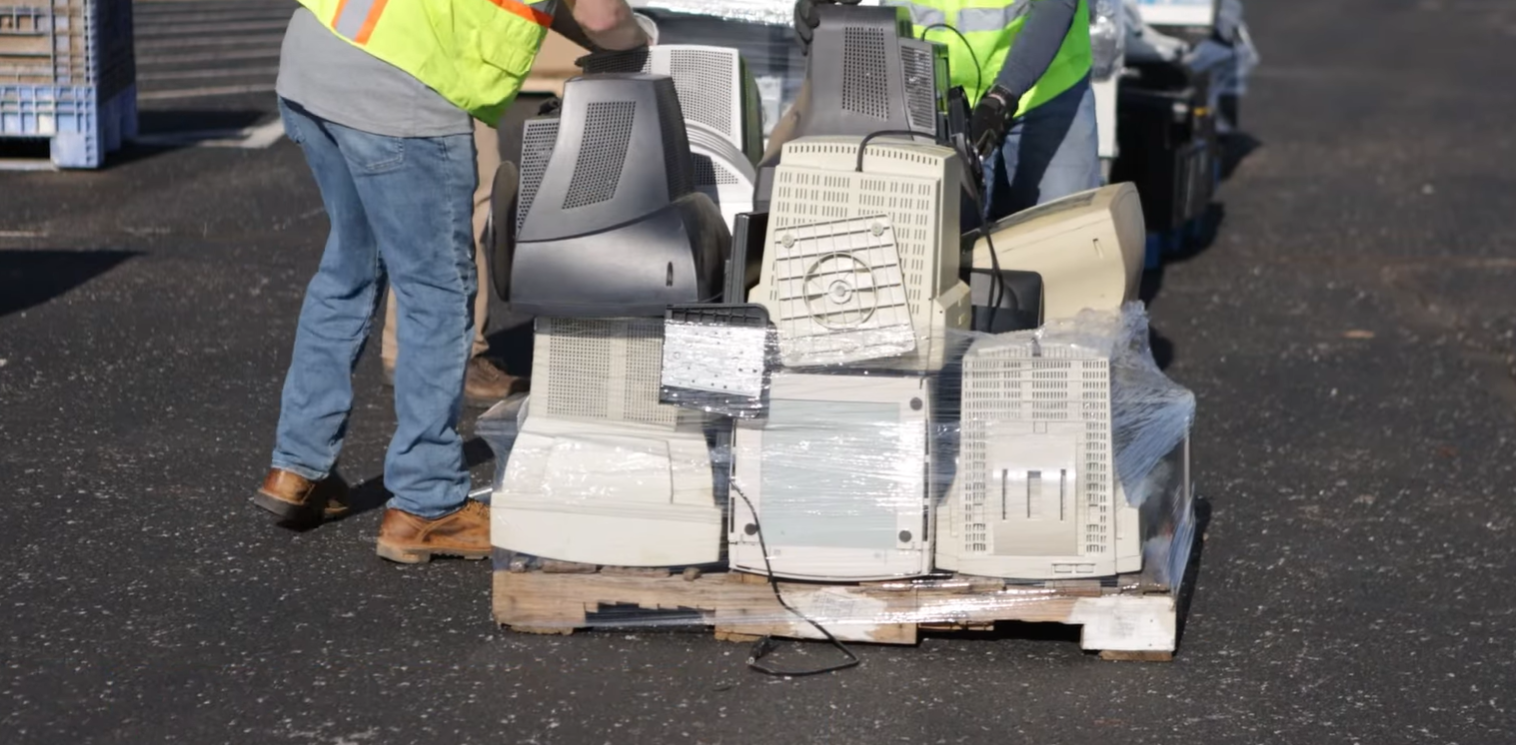 pallet of old computers with people stacking more