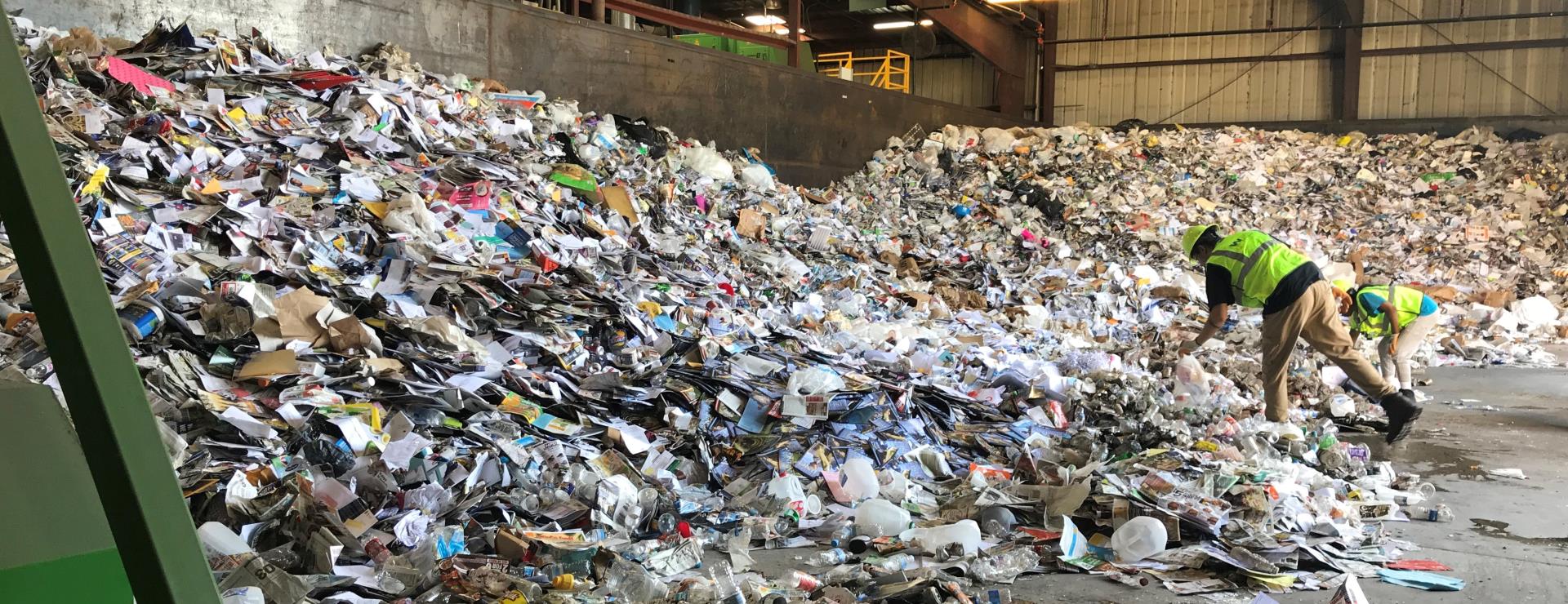 Contractor sorting through a mound of recycling in a warehouse.