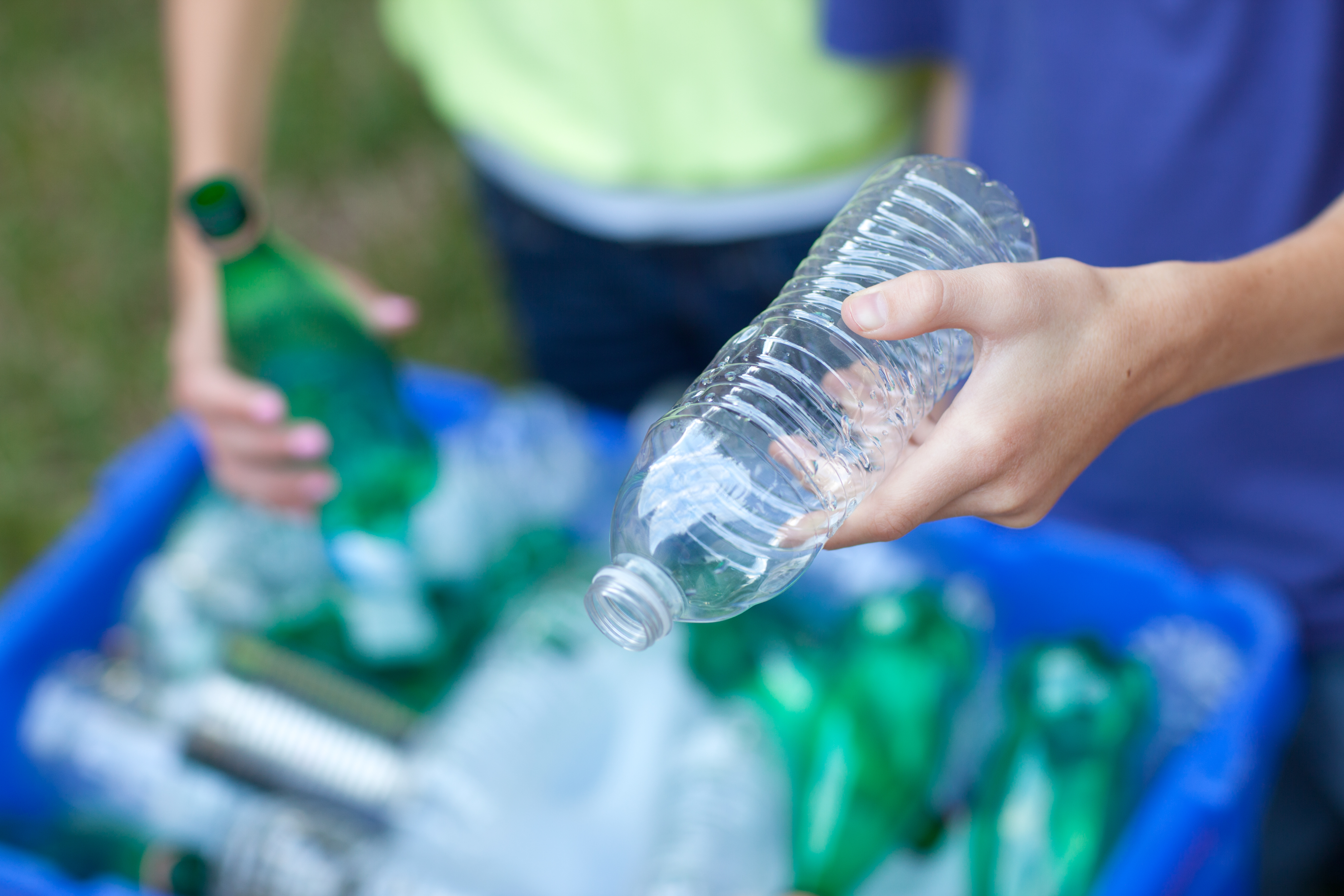 Two people hold empty plastic bottles above a tub filled with plastic bottles.