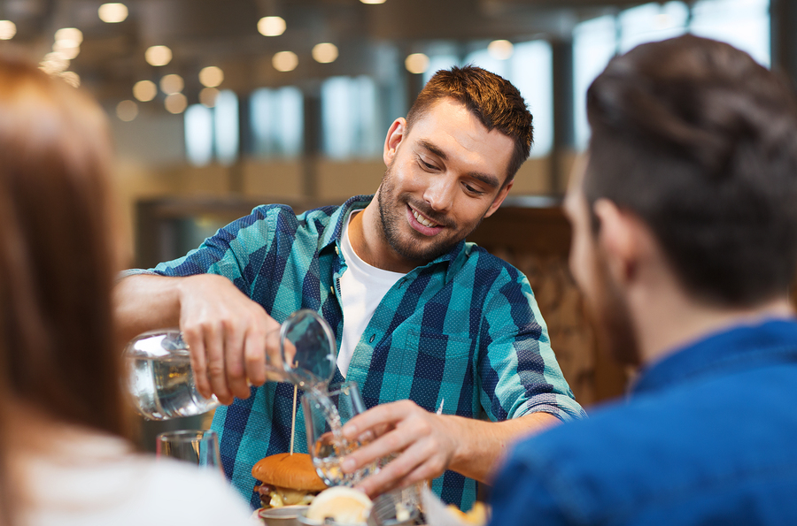 Photo of a man pouring water into a drinking glass at a restaurant.