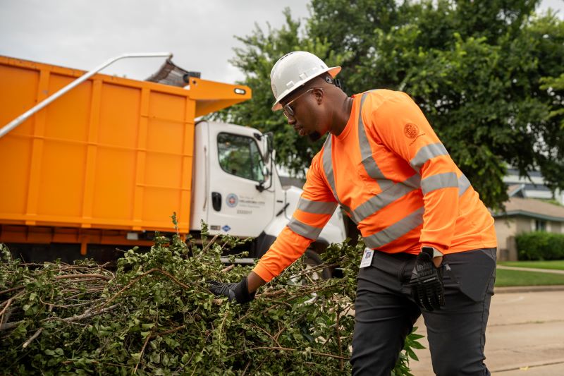 A bulky waste worker collects tree limbs from a resident's yard. 