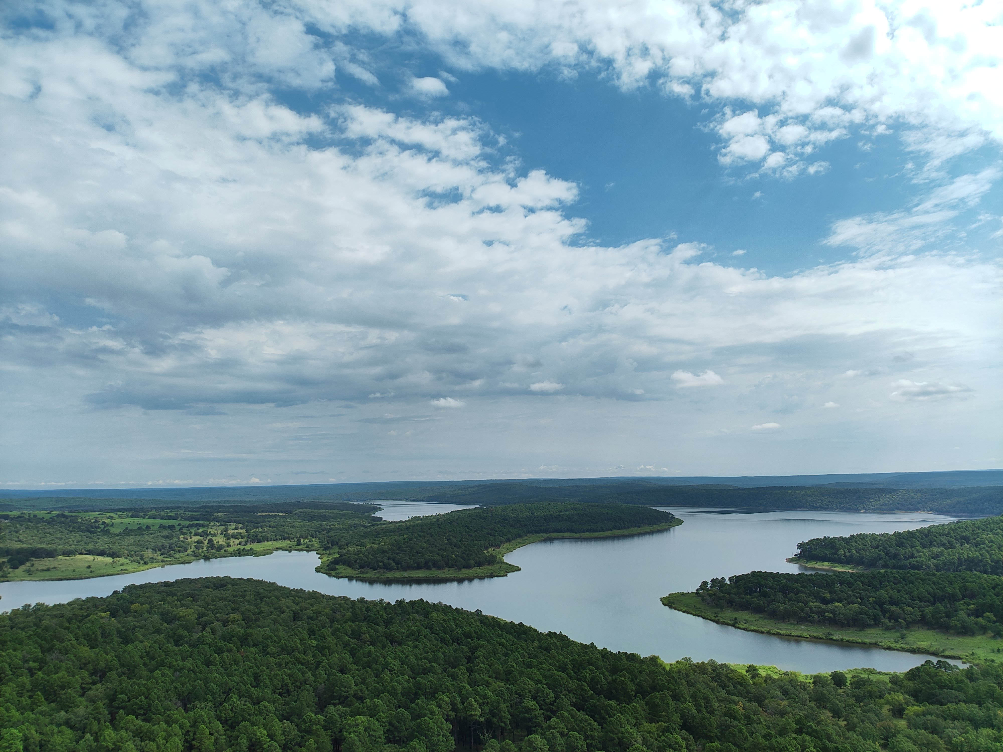 drone view of lake surrounded by green trees with blue cloudy skies