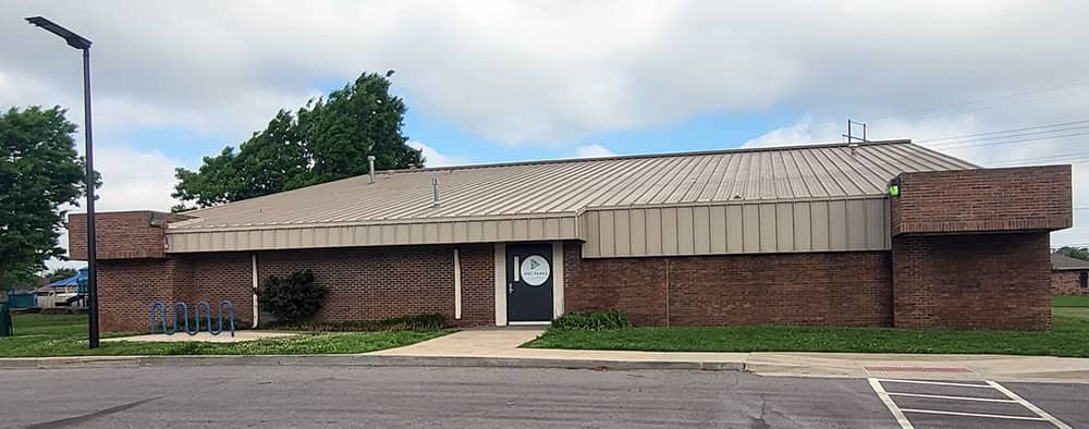 A brick building with tan roof under a blue and cloudy sky.